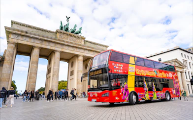 Red double-decker bus in front of Brandenburg Gate during Berlin Hop On & Hop Off tour.
