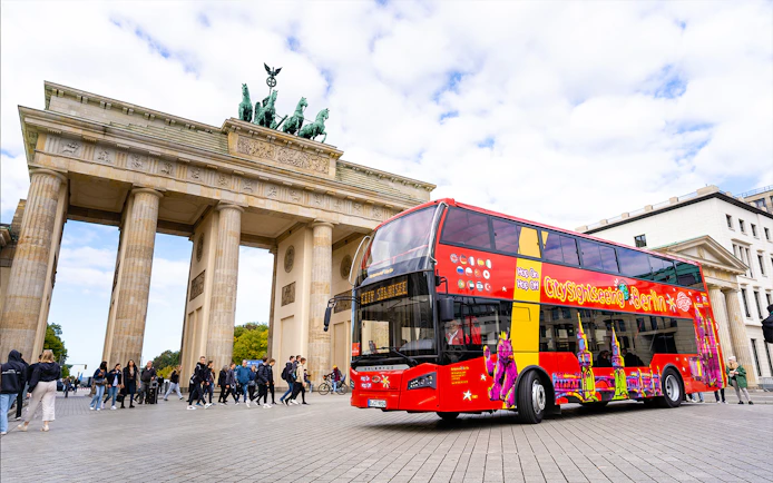 Red double-decker bus in front of Brandenburg Gate during Berlin Hop On & Hop Off tour.