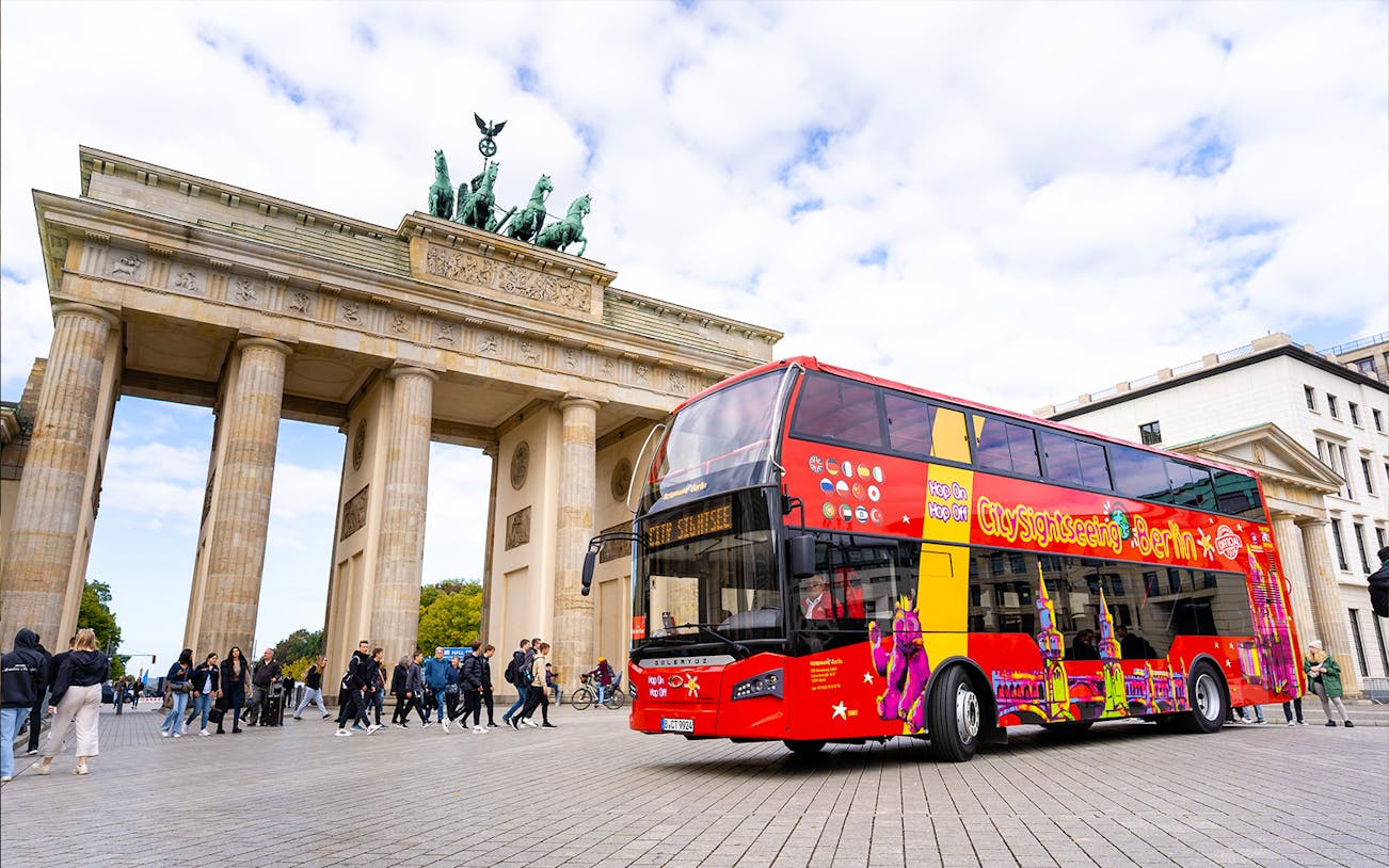 Red double-decker bus in front of Brandenburg Gate during Berlin Hop On & Hop Off tour.