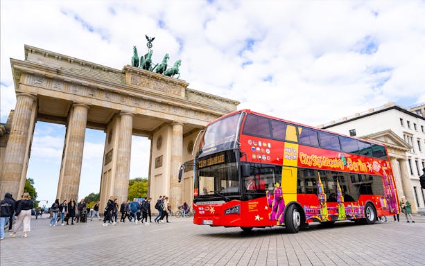 Red double-decker bus in front of Brandenburg Gate during Berlin Hop On & Hop Off tour.