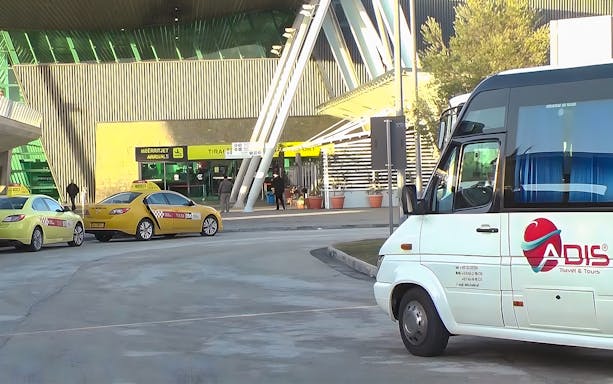 Bus and taxis at Tirana Airport entrance for Durres transfer service.