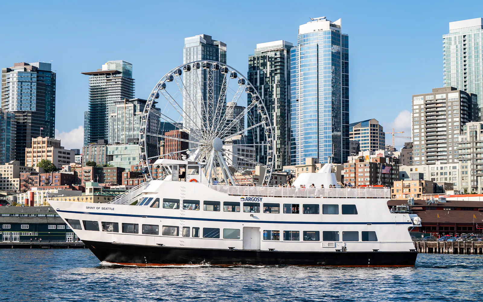 Argosy Cruise ship on Seattle waters with city skyline and Ferris wheel in the background.