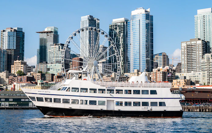 Argosy Cruise ship on Seattle waters with city skyline and Ferris wheel in the background.