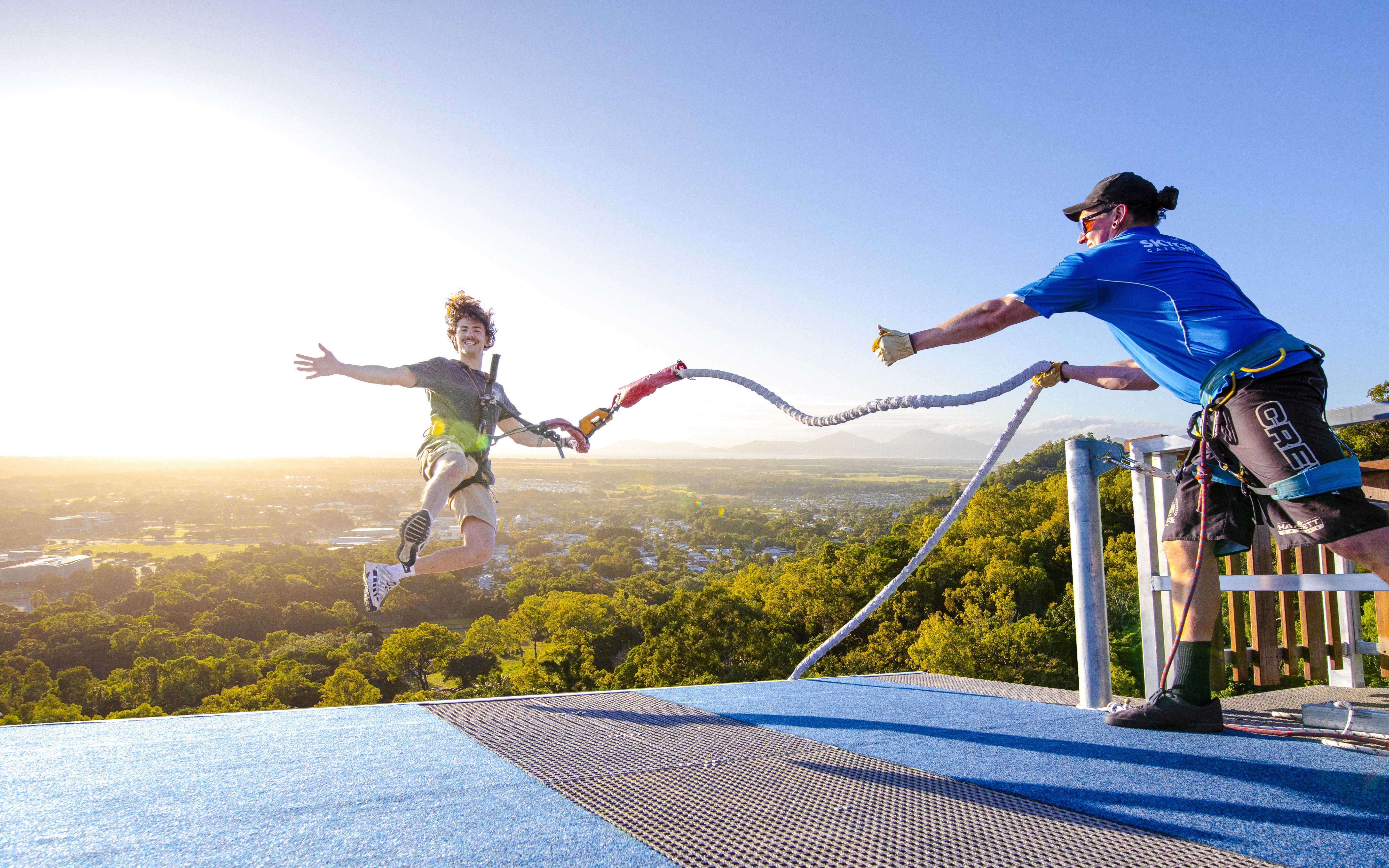 Person bungee jumping from rooftop with scenic city and mountain view.