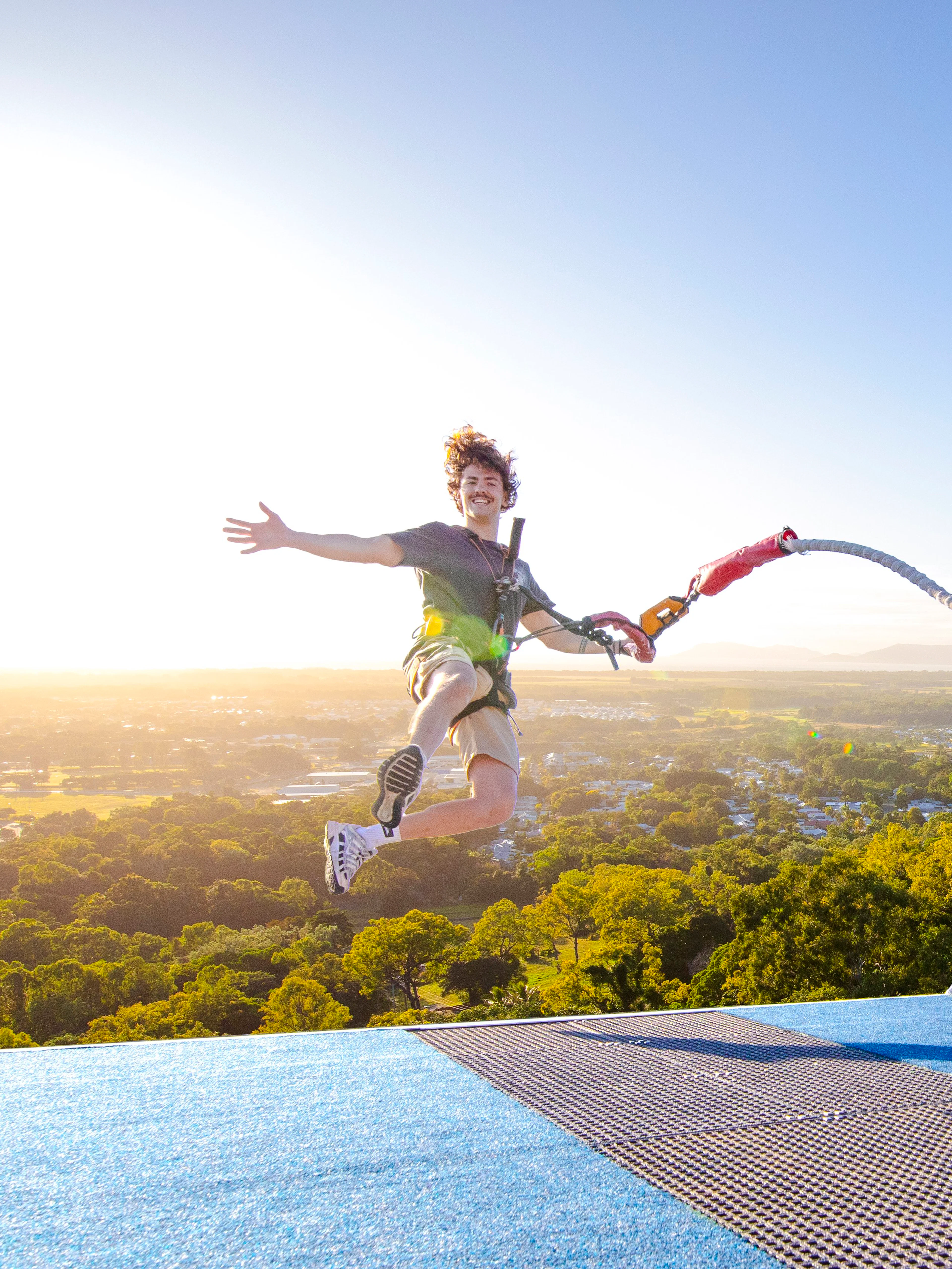 Person bungee jumping from rooftop with scenic city and mountain view.