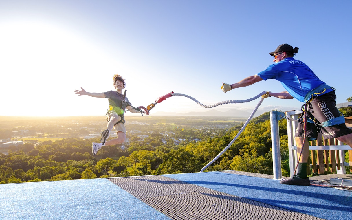 Person bungee jumping from rooftop with scenic city and mountain view.