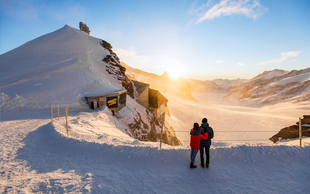 Couple enjoying sunrise view at Jungfraujoch, snowy landscape, Interlaken East trip.