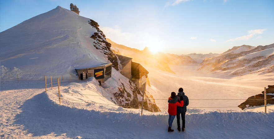 Couple enjoying sunrise view at Jungfraujoch, snowy landscape, Interlaken East trip.