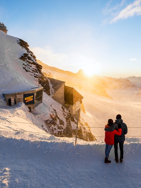 Couple enjoying sunrise view at Jungfraujoch, snowy landscape, Interlaken East trip.