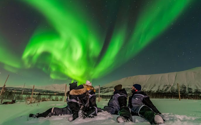 Group watching northern lights in snowy landscape, Norway.