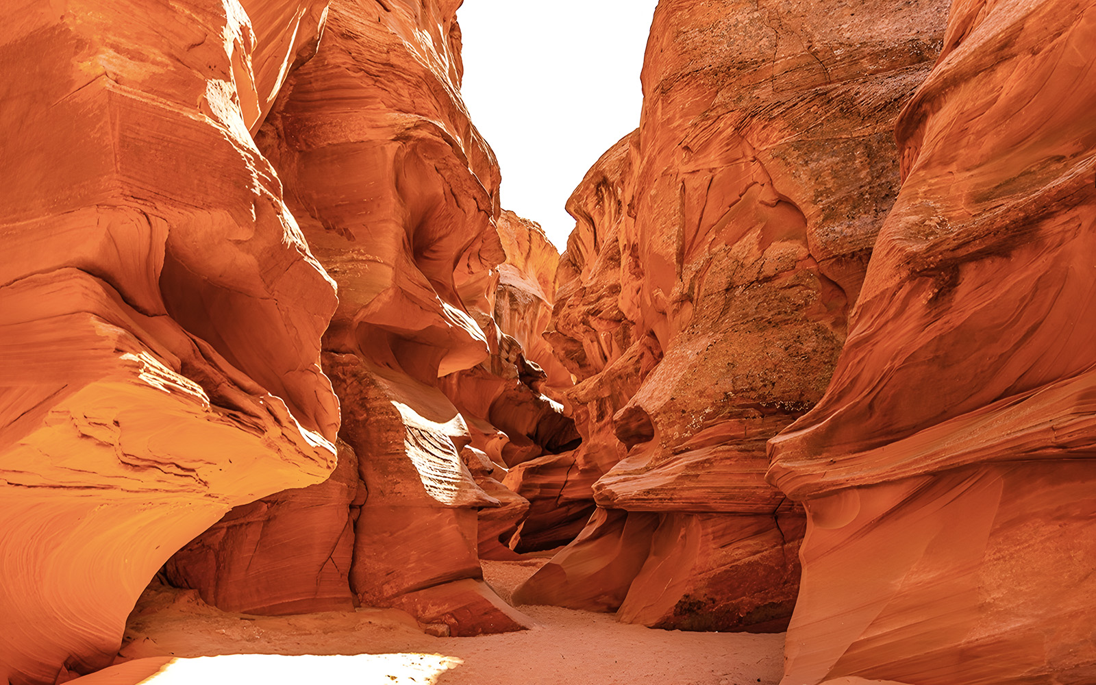 Waterhole Canyon's narrow sandstone passage with sunlight illuminating the red rock walls.