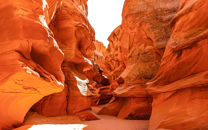 Waterhole Canyon's narrow sandstone passage with sunlight illuminating the red rock walls.