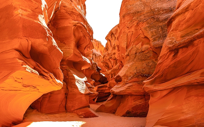 Waterhole Canyon's narrow sandstone passage with sunlight illuminating the red rock walls.