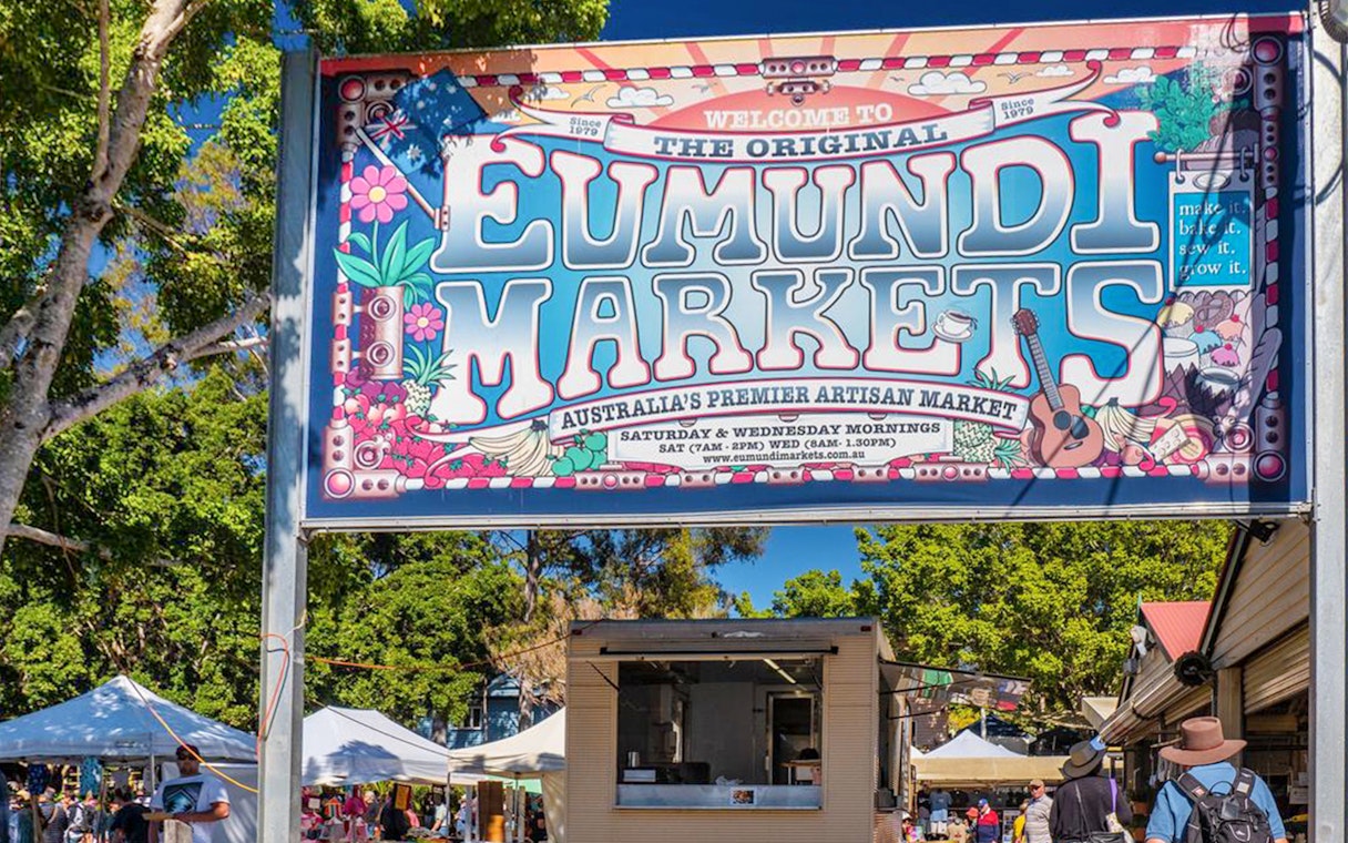 Eumundi Markets entrance sign with visitors and market stalls in Eumundi, Australia.