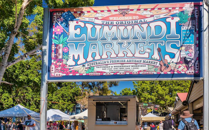 Eumundi Markets entrance sign with visitors and market stalls in Eumundi, Australia.