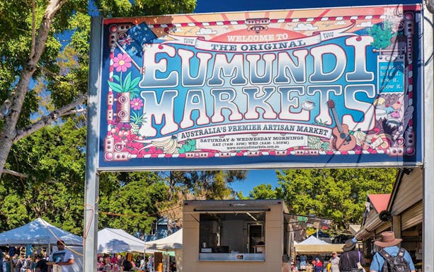 Eumundi Markets entrance sign with visitors and market stalls in Eumundi, Australia.