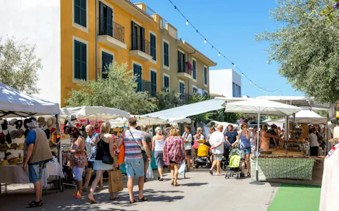 Artà country market in Majorca, Spain with people browsing stalls under umbrellas.