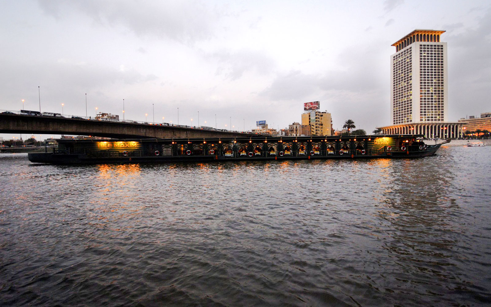 Luxury dinner cruise boat on the Nile River near Cairo bridge at dusk.