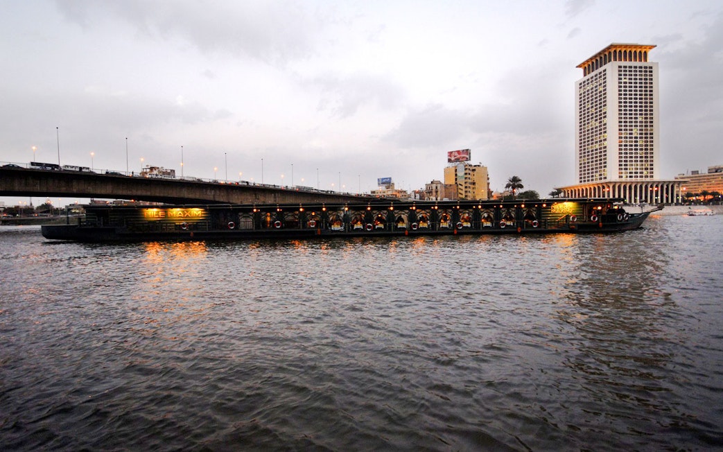 Luxury dinner cruise boat on the Nile River near Cairo bridge at dusk.