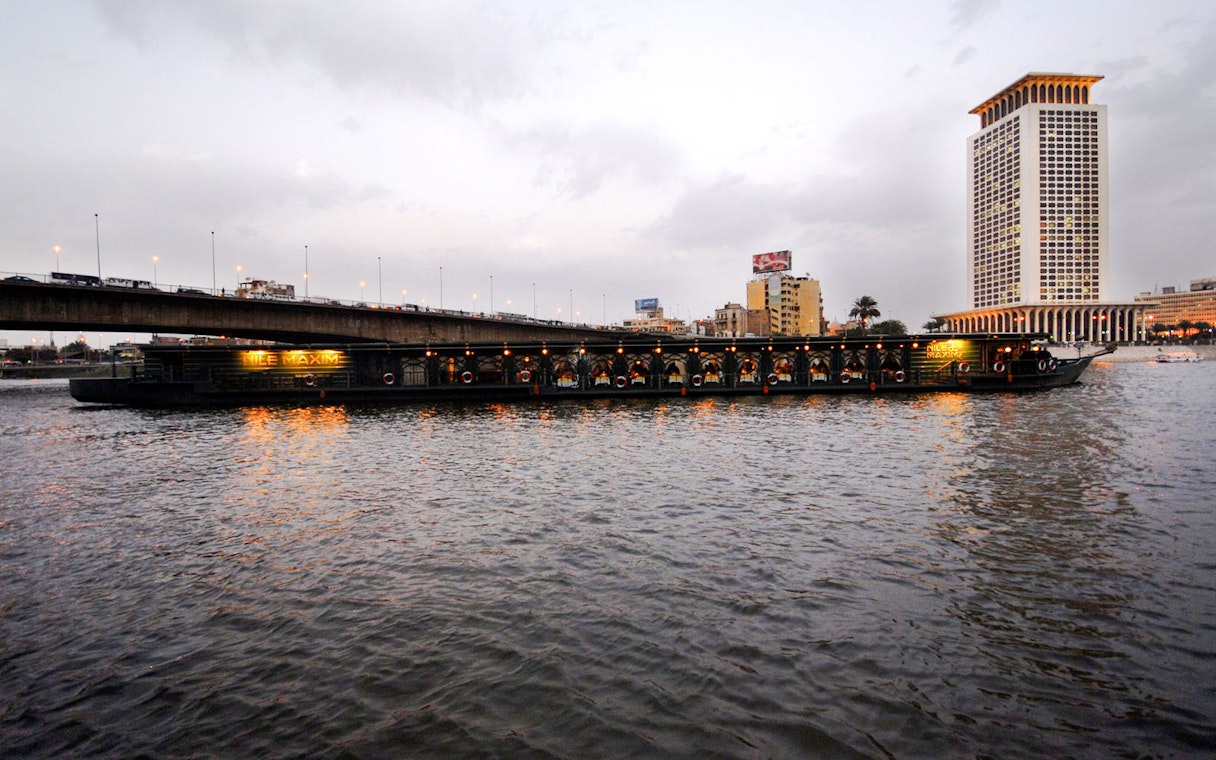 Luxury dinner cruise boat on the Nile River near Cairo bridge at dusk.