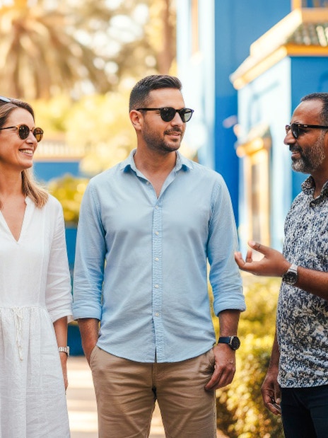 Guide with tourists in Jardin Majorelle, Marrakech, near blue building.
