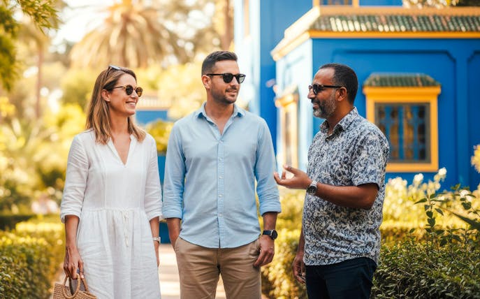 Guide with tourists in Jardin Majorelle, Marrakech, near blue building.