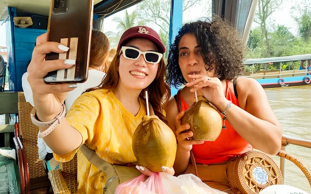 Tourists enjoying fresh coconuts on a boat during Mekong Delta day tour from Ho Chi Minh.