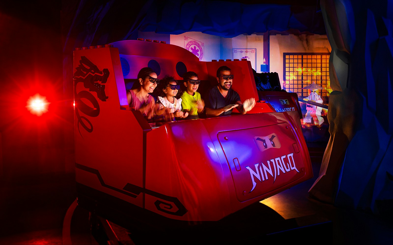 Visitors enjoying NINJAGO ride at LEGOLAND Florida, wearing 3D glasses in a themed vehicle.