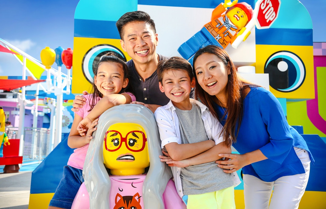 Family enjoying a day at LEGOLAND® California with colorful LEGO figures in the background.