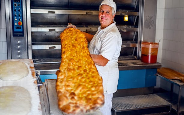 Baker holding large pizza in Rome bakery during food tour.