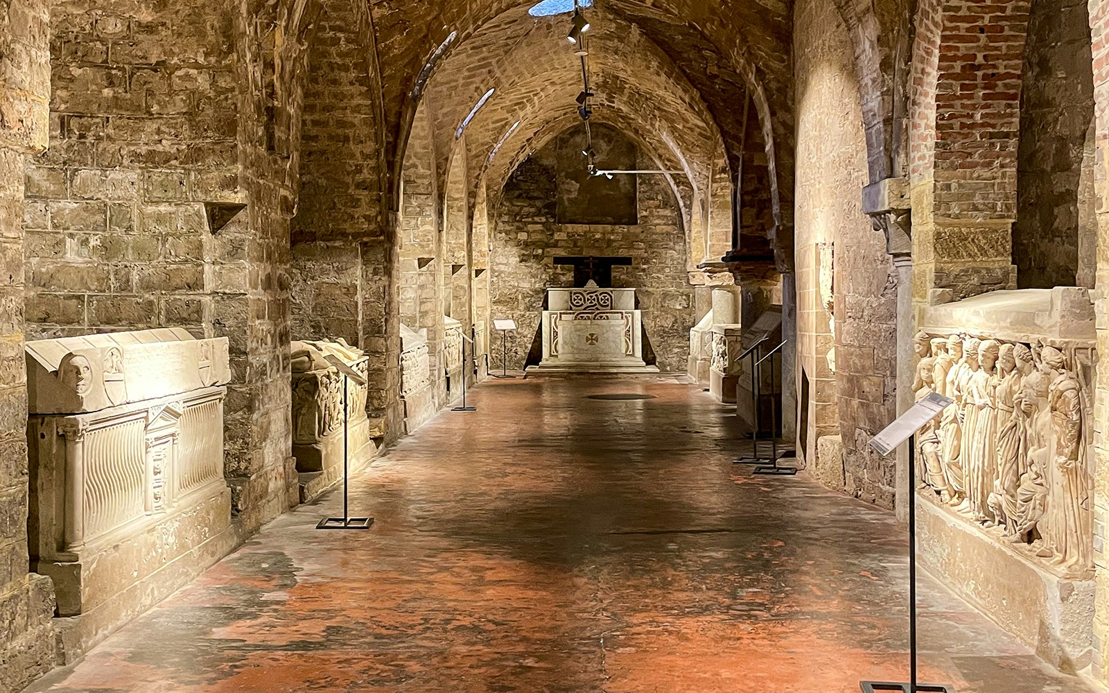 Crypt interior of Palermo Cathedral with stone sarcophagi and arched ceilings.