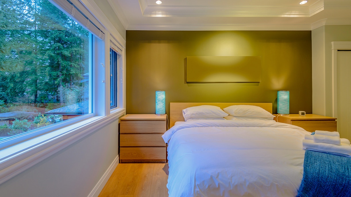 Luxury hotel room with a large bed, modern decor, and forest view through a wide window.