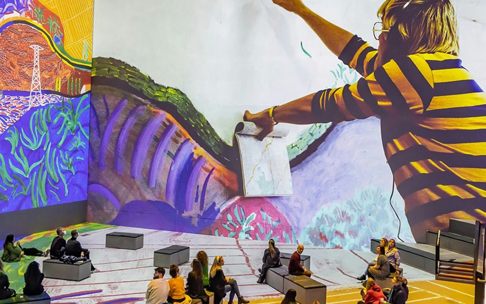 Interactive exhibit of David Hockney's art with visitors seated, titled "Bigger & Closer.