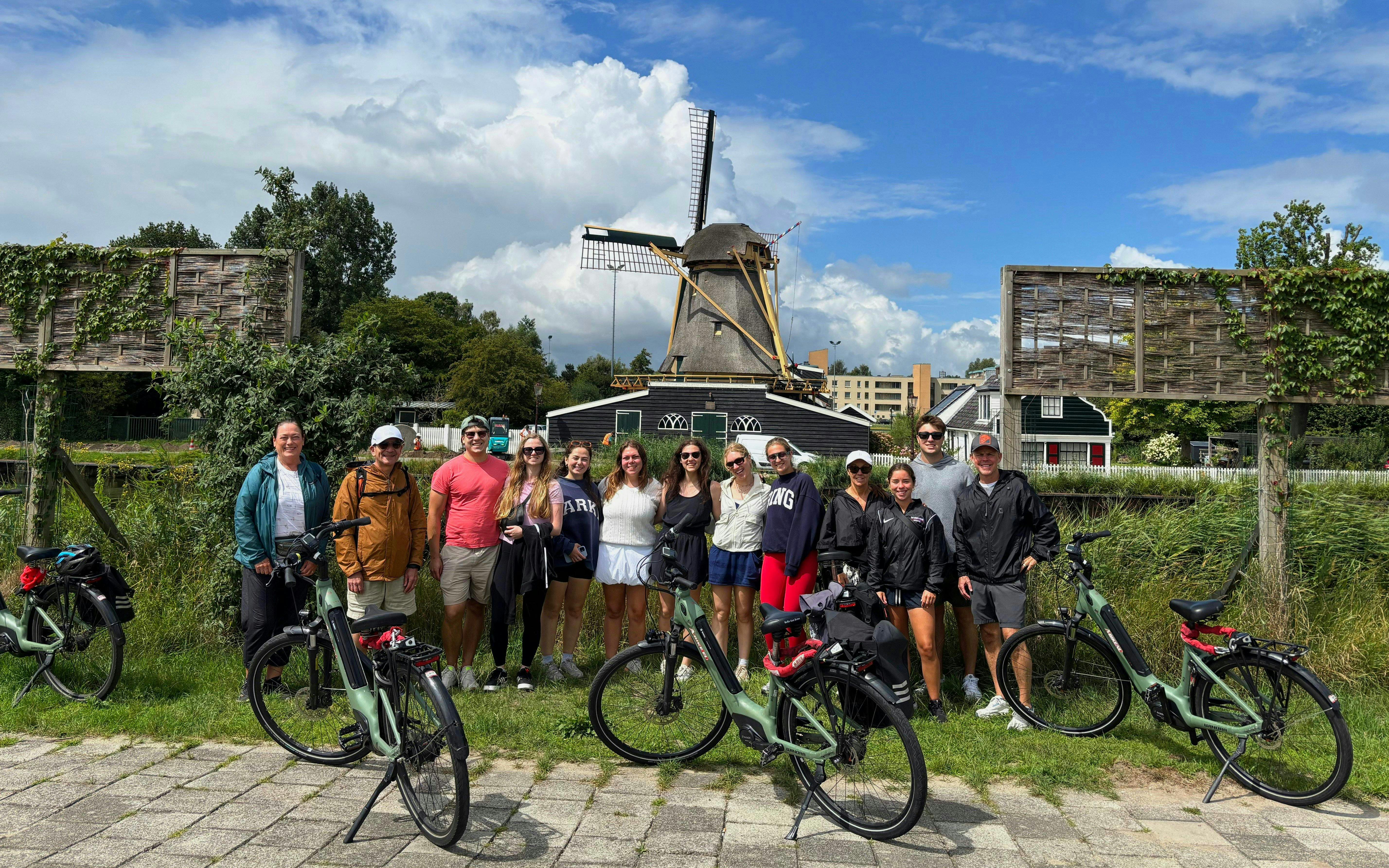 Group on e-bike tour in front of a traditional windmill in the Netherlands.