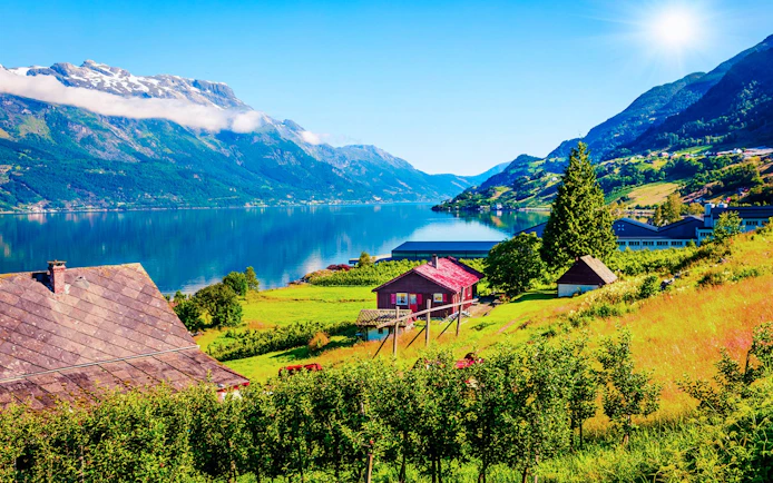 Øystese village along Hardangerfjord in Norway with houses, greenery, and mountains.