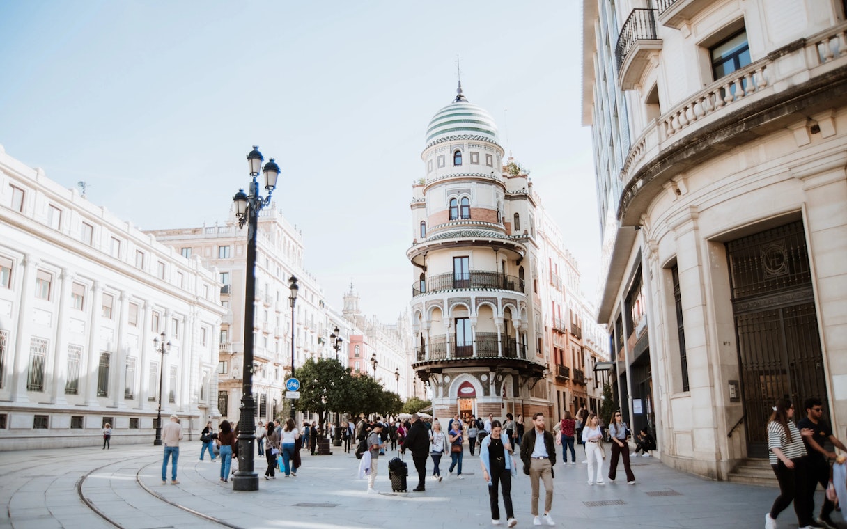 Street in Seville, Spain, showcasing unique round building and bustling pedestrian activity.