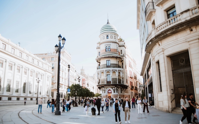 Street in Seville, Spain, showcasing unique round building and bustling pedestrian activity.