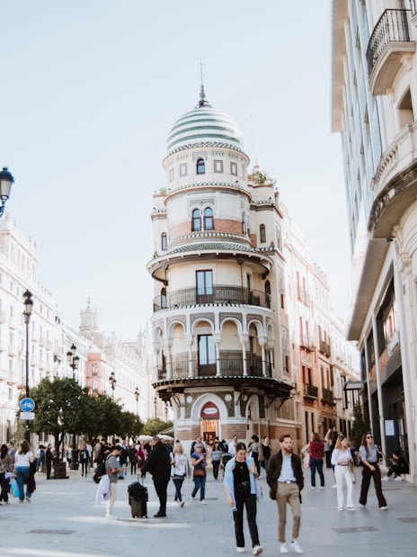 Street in Seville, Spain, showcasing unique round building and bustling pedestrian activity.