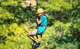 Person ziplining through forest with safety gear and helmet.