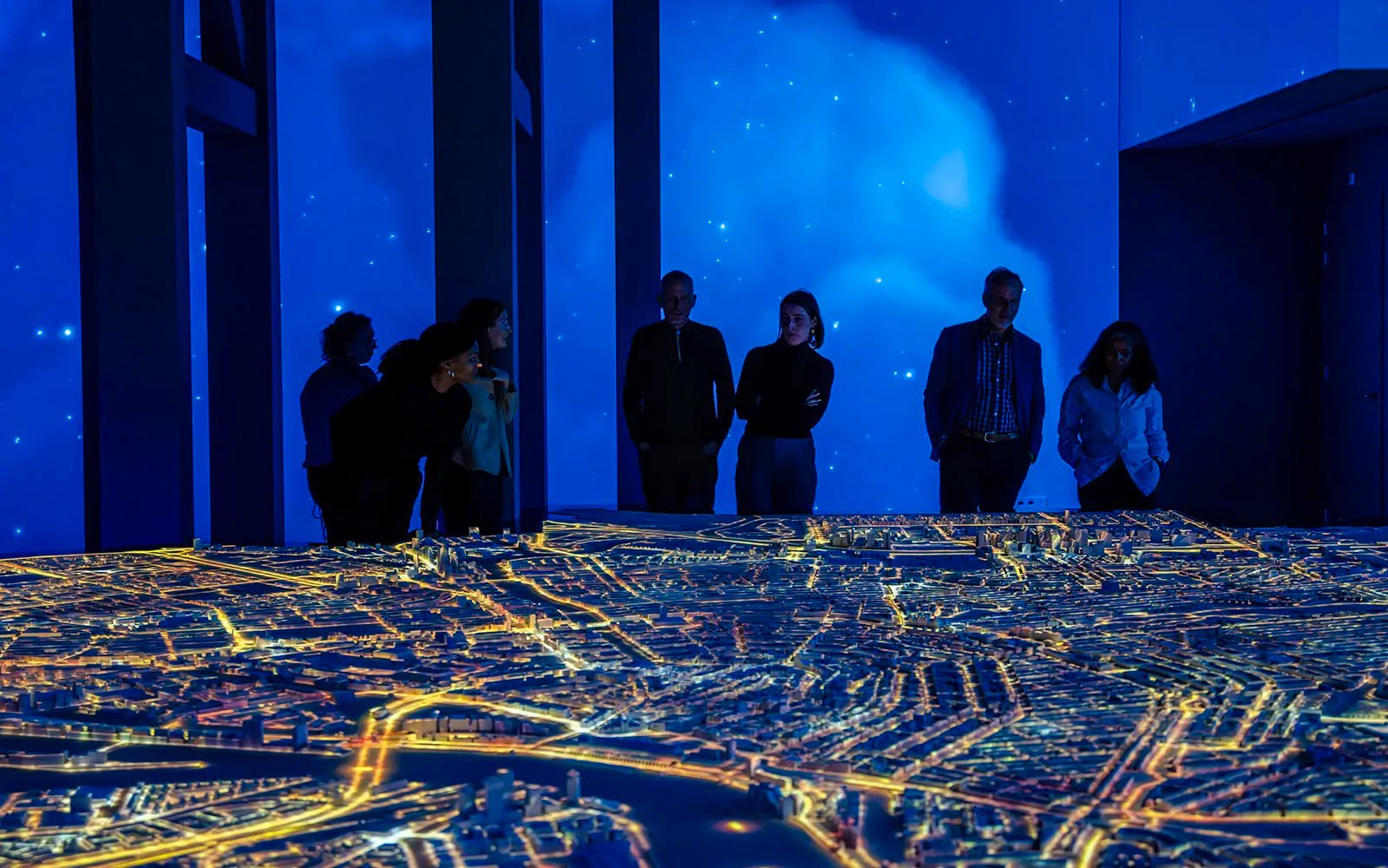 Visitors observing illuminated Amsterdam city model at the Amsterdam in Motion exhibit.