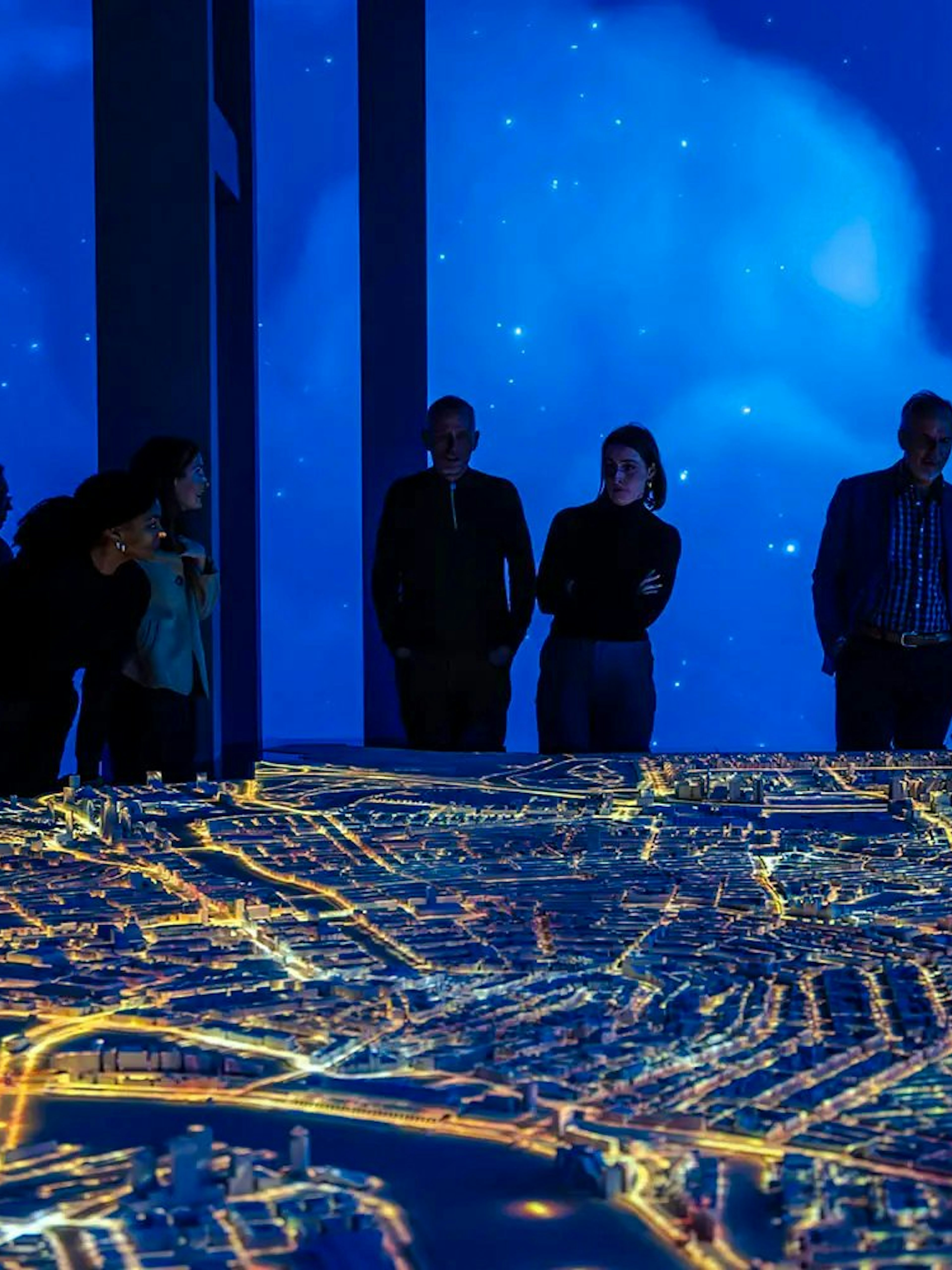 Visitors observing illuminated Amsterdam city model at the Amsterdam in Motion exhibit.