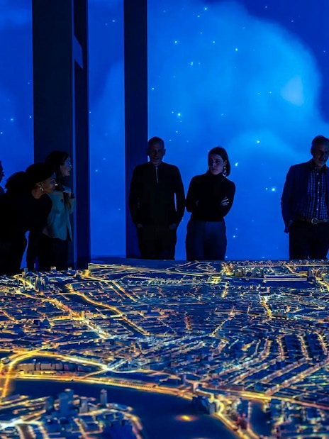 Visitors observing illuminated Amsterdam city model at the Amsterdam in Motion exhibit.