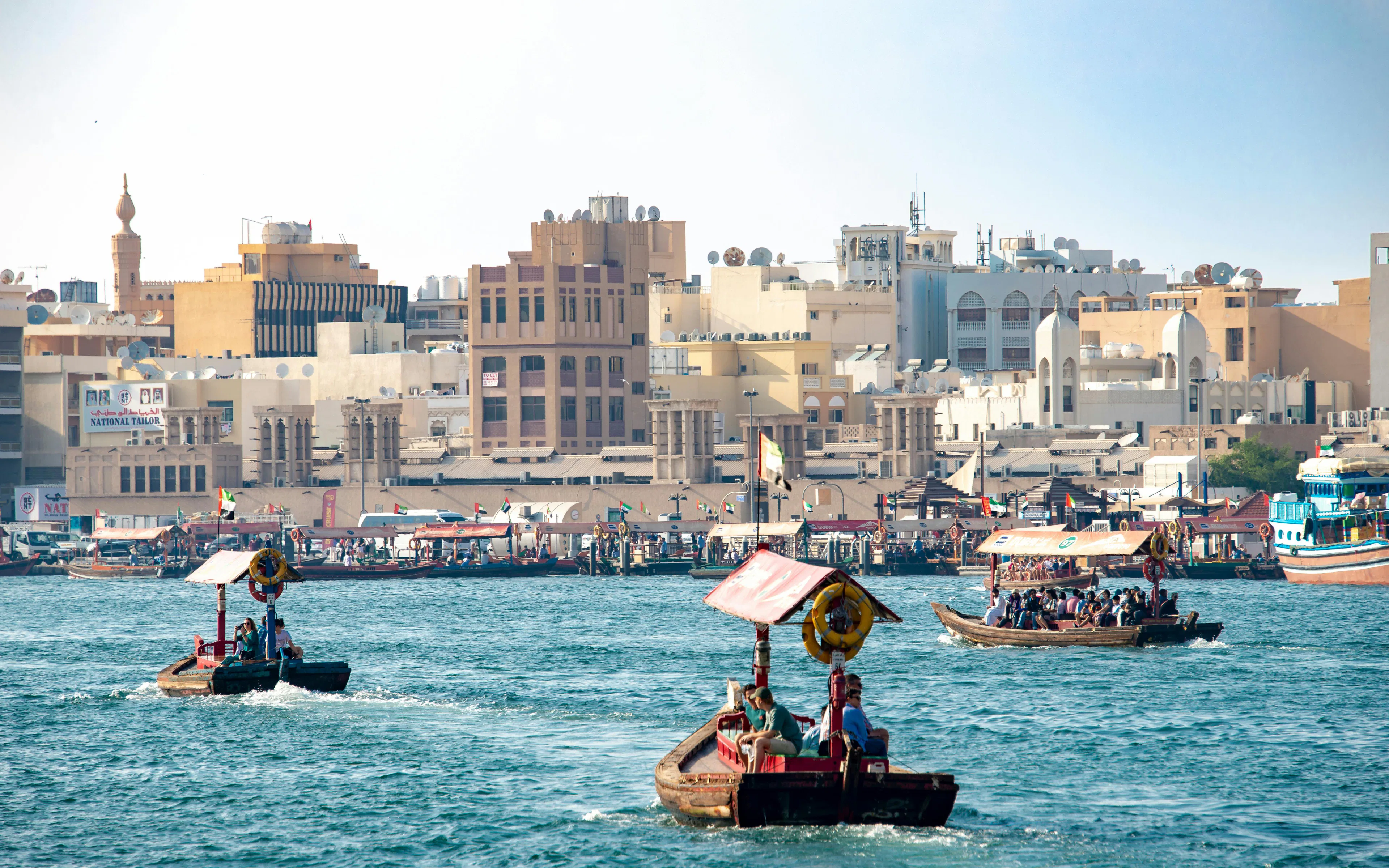 Traditional water taxis, abras, crossing Dubai Creek towards Deira with cityscape in background.