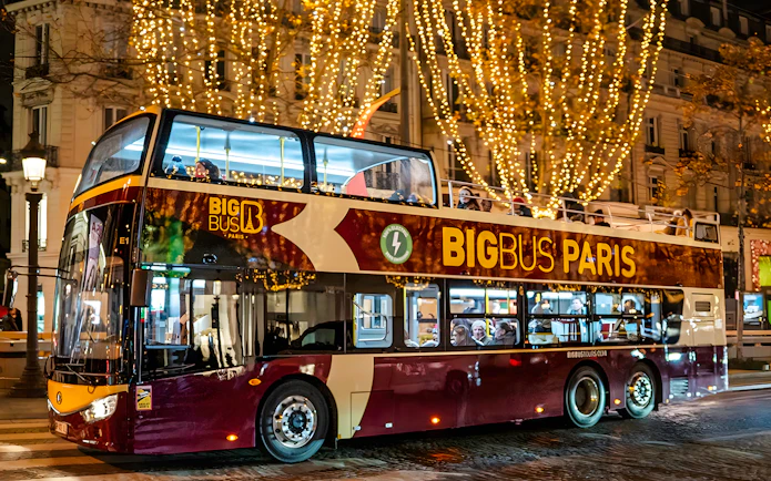 Paris hop-on hop-off bus with Christmas lights at night.