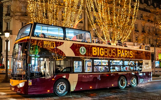 Paris hop-on hop-off bus with Christmas lights at night.