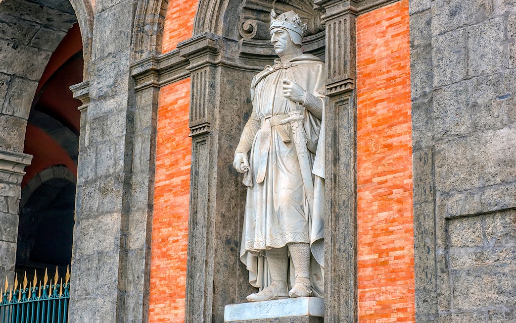 Statue of a crowned figure in the Royal Palace of Naples gardens.