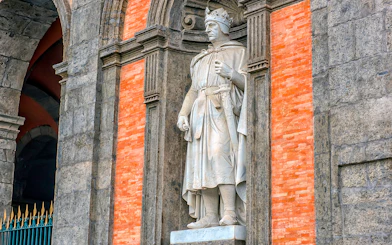 Statue of a crowned figure in the Royal Palace of Naples gardens.