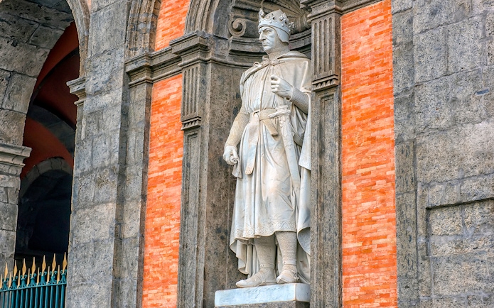 Statue of a crowned figure in the Royal Palace of Naples gardens.