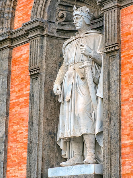 Statue of a crowned figure in the Royal Palace of Naples gardens.