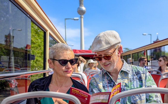 Participants on a Big Bus Berlin tour reading brochures with the TV Tower in the background.